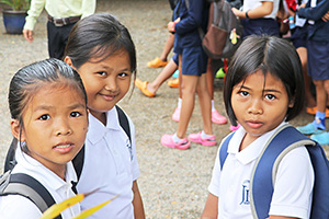 JPA Image Gallery - Primary students smile as they wait with their bookbags - Jay Pritzker Academy, Siem Reap, Cambodia