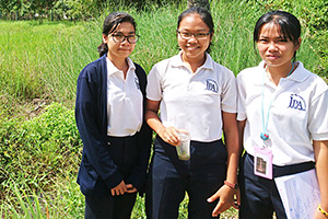 JPA Image Gallery - 3 high school students stand in a grassy area - Jay Pritzker Academy, Siem Reap, Cambodia