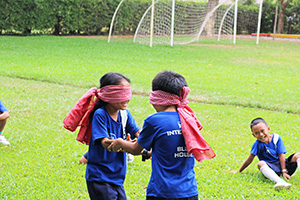 JPA Image Gallery - 2 primary students in blindfolds laugh as they find each other - Jay Pritzker Academy, Siem Reap, Cambodia