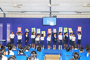 JPA Image Gallery - Primary students hold up letter cards spelling compassion at assembly - Jay Pritzker Academy, Siem Reap, Cambodia