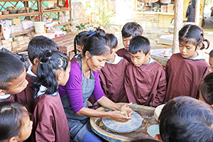 JPA Image Gallery - Primary students watch potter explain the pottery wheel while on field trip - Jay Pritzker Academy, Siem Reap, Cambodia