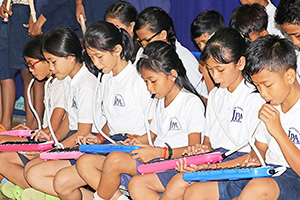 JPA Image Gallery - Primary students play air pianos and recorders at assembly musical performance - Jay Pritzker Academy, Siem Reap, Cambodia