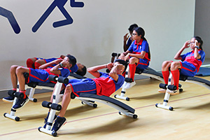 JPA Image Gallery - High school students in sports uniform do crunches on gym equipment  - Jay Pritzker Academy, Siem Reap, Cambodia