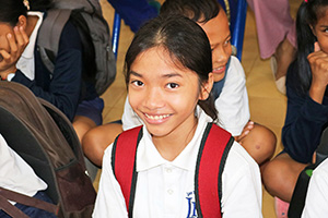 JPA Image Gallery - Primary student smiles while waiting at assembly - Jay Pritzker Academy, Siem Reap, Cambodia