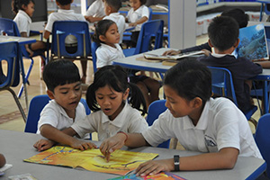 JPA Image Gallery - An older student assists younger students as they read a book together - Jay Pritzker Academy, Siem Reap, Cambodia