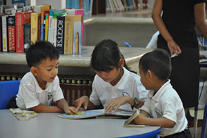 JPA Image Gallery - Primary students examine a map in a book together at the library - Jay Pritzker Academy, Siem Reap, Cambodia
