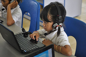 JPA Image Gallery - A primary student reads the computer screen, ready to make a selection with the mouse - Jay Pritzker Academy, Siem Reap, Cambodia