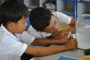 JPA Image Gallery - Primary students measure liquid in a jar and use a magnifying glass - Jay Pritzker Academy, Siem Reap, Cambodia