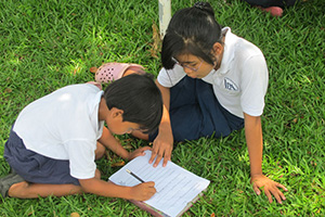 JPA Image Gallery - Primary students write their answers on a worksheet outdoors - Jay Pritzker Academy, Siem Reap, Cambodia
