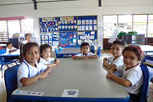 JPA Image Gallery - Primary students smile at their table - Jay Pritzker Academy, Siem Reap, Cambodia